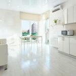 Světlý minimalistický byt s bílým nábytkem, stolem u okna a výhledem na město.