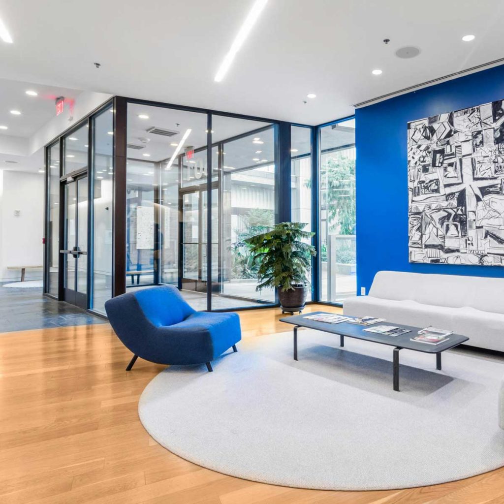 Moderní kancelářský prostor s posezením, skleněnými stěnami a modrým akcentem.