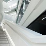 Moderní schodiště v budově s bílým interiérem a liniovým osvětlením