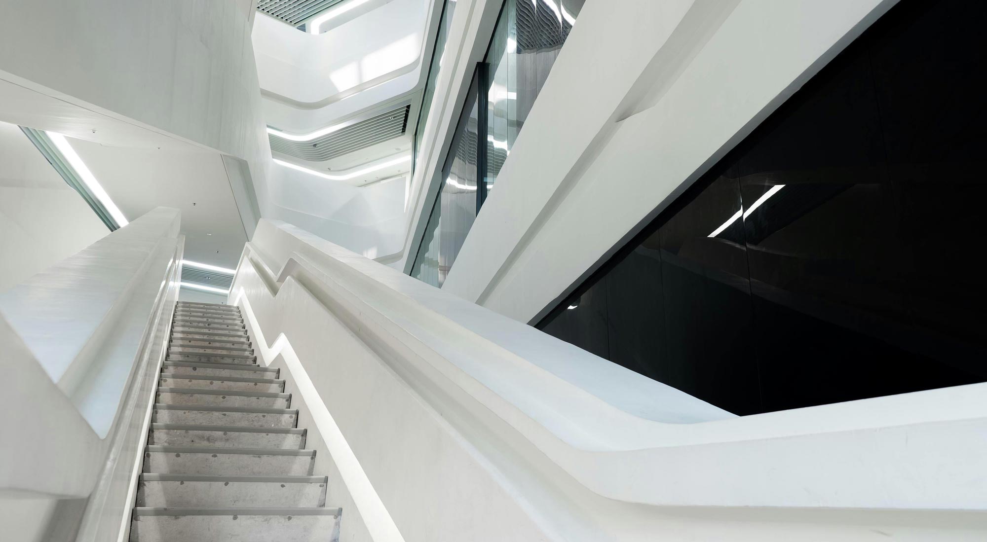 Moderní schodiště v budově s bílým interiérem a liniovým osvětlením