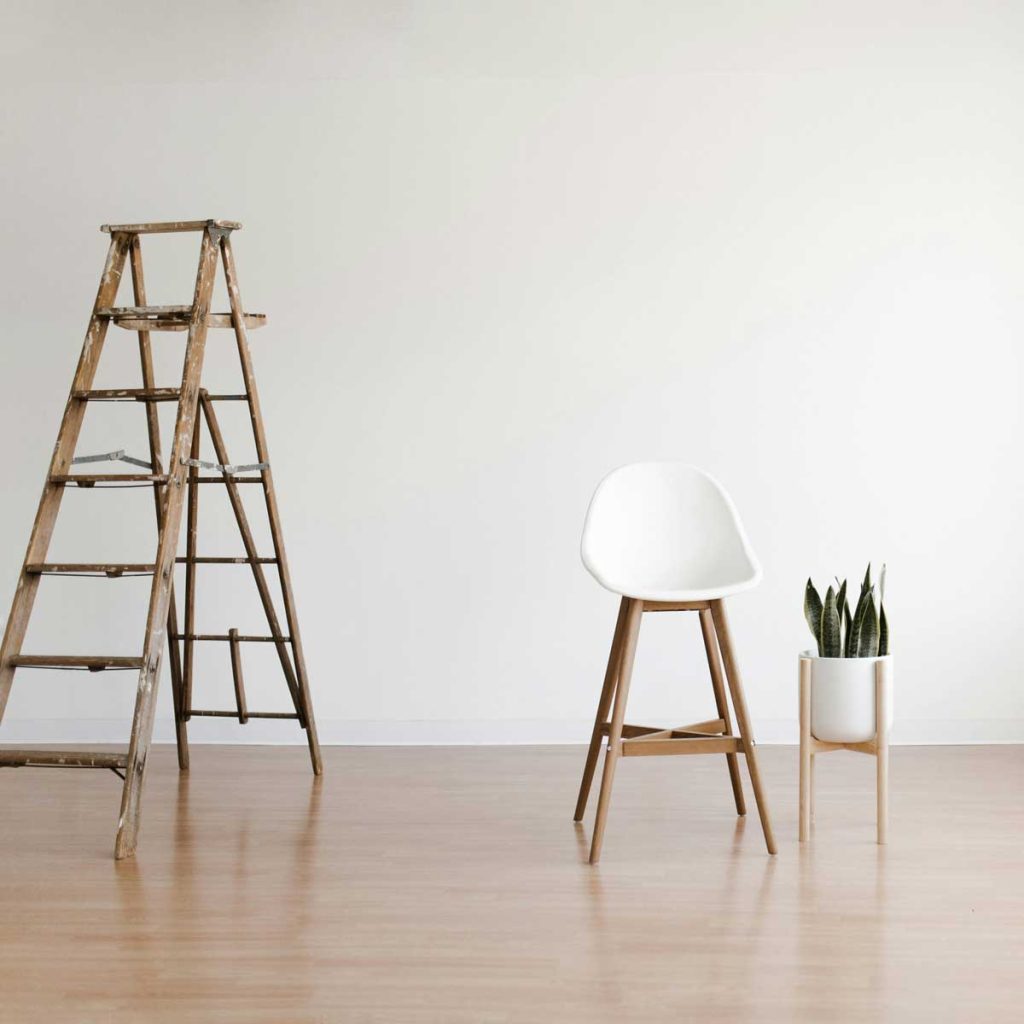 Minimalistický interiér s dřevěnou podlahou, židlí, žebříkem a květinou.